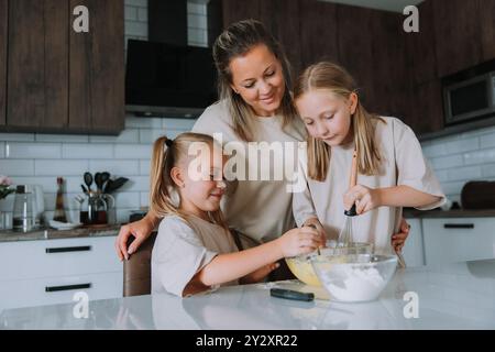 deux petites filles avec leur mère cuisinent une tarte à la maison dans la cuisine. Photo de haute qualité Banque D'Images