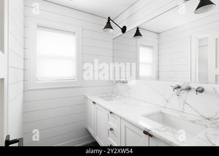 Une salle de bains de style ferme avec des murs de shiplap, un meuble de toilette flottant blanc et des lumières montées au-dessus du miroir. Banque D'Images