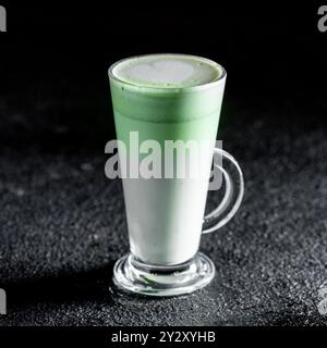 Un verre de latte matcha avec un motif coeur sur le dessus vert mousseux debout sur une surface texturée sombre. Banque D'Images