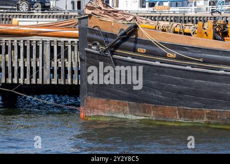 Une vue rapprochée de la proue d'un bateau en bois vintage amarré à une marina. Le bateau dispose d'une coque sombre avec un aspect altéré, attaché à un pi en bois Banque D'Images