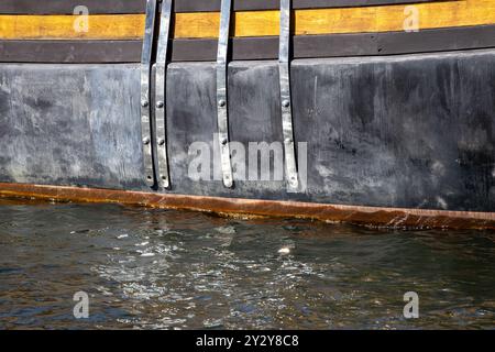 Gros plan de la coque d'un bateau montrant des fixations métalliques et des accents en bois, partiellement immergé dans l'eau. Banque D'Images
