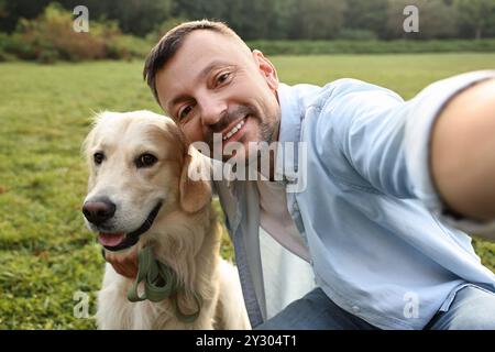 Homme souriant avec chien mignon Golden Retriever prenant selfie le jour du printemps Banque D'Images