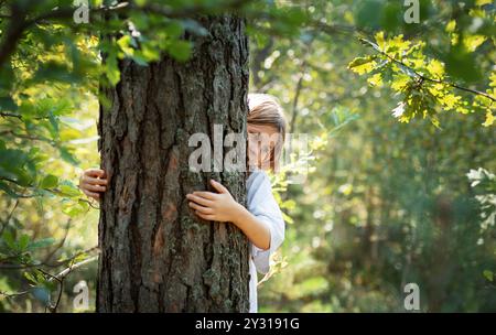 Une adolescente embrasse un arbre dans la forêt. Embrasser et toucher les arbres pour réduire le stress et se connecter avec la nature. Banque D'Images