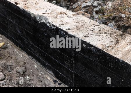 Nouveau mur de fondation en bande en béton armé est recouvert d'une composition de bitume noir protecteur, maison rurale est en construction Banque D'Images