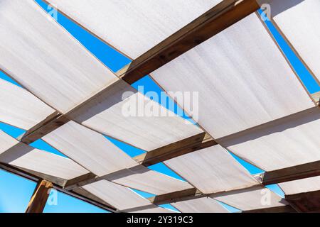 Toit de terrasse fait de bandes de tissu blanc sur cadre en bois est sous ciel bleu Banque D'Images