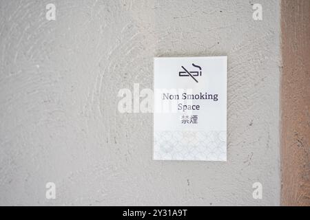 Panneau carré blanc non fumeur de papier sur un mur dans un lieu public. Le signe non fumeur est la ligne noire croisée fumée de cigarette avec la lettre anglaise et chinoise me Banque D'Images
