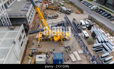 Vue aérienne d'un chantier de construction présentant des grues, des véhicules de construction et des matériaux de construction. Ouvriers de la construction enlevant la grande grue avec sma Banque D'Images