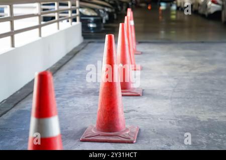 Cônes orange vif se tenant dans une rangée au parking. Portrait d'un cône de circulation orange est aligné sur le parking à plusieurs étages. Banque D'Images