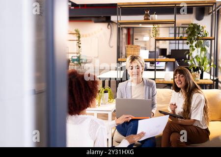 Utilisation d'un ordinateur portable et d'une tablette pour des entreprises créatives, des femmes multiraciales collaborant dans un bureau moderne Banque D'Images