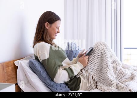 À la maison, se détendre au lit, femme lisant sur tablette enveloppée dans une couverture confortable Banque D'Images