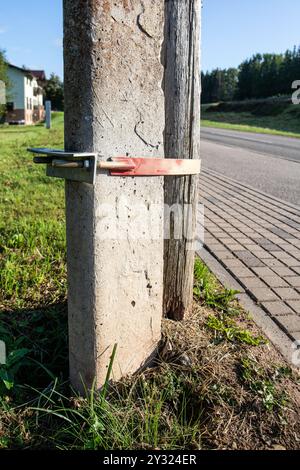 Une bûche en bois attachée à un poteau en béton avec un tendeur. Fixation du pôle électrique. Banque D'Images