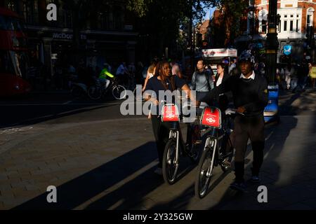 Un jeune homme et une jeune femme poussant une paire de Santander cycles, Cambridge Circus, Londres, Royaume-Uni. 9 août 2023 Banque D'Images