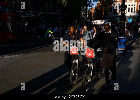 Un jeune homme et une jeune femme poussant une paire de Santander cycles, Cambridge Circus, Londres, Royaume-Uni. 9 août 2023 Banque D'Images