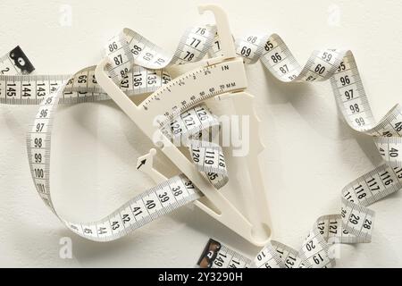 Pied à coulisse en plastique et ruban à mesurer sur table blanche, vue de dessus Banque D'Images