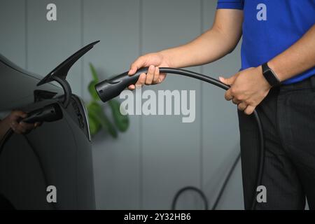 Homme méconnaissable branchant dans une voiture électrique. Concept d'énergie renouvelable et de transport Banque D'Images