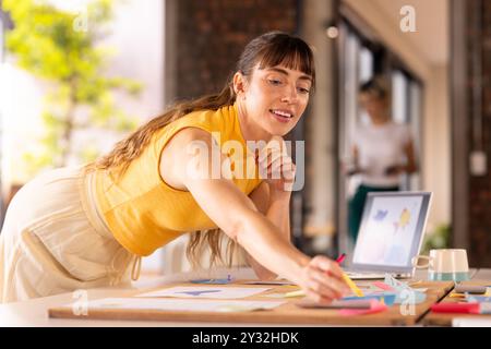 Au bureau, écrivant sur des notes adhésives, femme remue des idées au bureau avec un ordinateur portable Banque D'Images