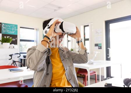 À l'aide d'un casque VR, adolescent asiatique excité expérimentant la réalité virtuelle dans la salle de classe de l'école. Technologie, éducation, apprentissage, innovation, expérience, Banque D'Images