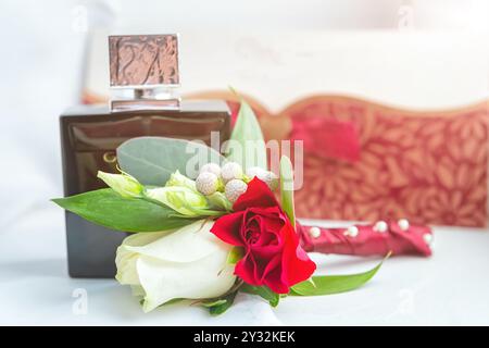 Une collection d'accessoires de mariage comprend une bouteille de parfum élégante, une boutonnière florale et un noeud papillon classique reposant sur un rebord de fenêtre. Banque D'Images