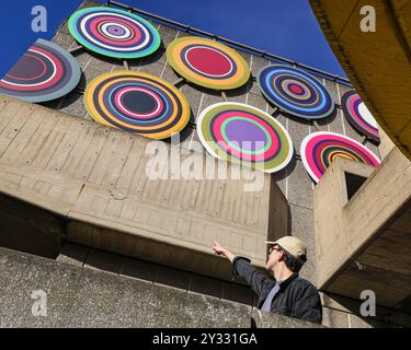 Londres, Royaume-Uni. 12 septembre 2024. Un membre du personnel pose avec le travail. Dévoilement officiel de « Target Queen », la première œuvre en plein air de l'artiste acclamé Bharti Kher dans une institution londonienne. La commission a été positionnée sur les façades est et sud de la Hayward Gallery, célébrant et interagissant de manière ludique avec l'architecture emblématique du Southbank Centre. Il comporte des bindis à grande échelle, traditionnellement utilisés par les femmes sud-asiatiques comme symboles culturels désignant le troisième œil. Crédit : Imageplotter/Alamy Live News Banque D'Images