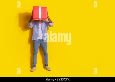 Photo pleine longueur de funky cool Guy habillé chemise à carreaux tenant grand rouge présent emtpy espace isolé fond de couleur jaune Banque D'Images