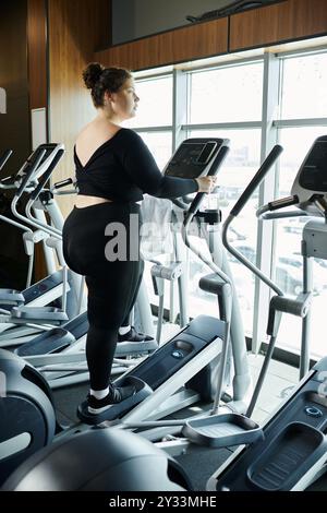 Une femme de grande taille s'entraîne en toute confiance à la salle de sport, embrassant la positivité corporelle dans des vêtements actifs élégants. Banque D'Images