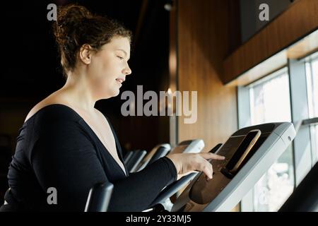 Une jeune femme de grande taille s'entraîne en toute confiance sur un elliptique, célébrant son parcours de remise en forme. Banque D'Images