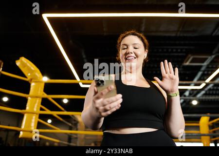 Une femme de grande taille aime sa routine d'entraînement, se connectant joyeusement sur son téléphone dans un environnement de gymnastique énergique. Banque D'Images