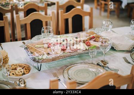 Une table à manger magnifiquement sertie avec un plateau d'entrées recouvert d'un film plastique, mettant en vedette diverses viandes, fromages et légumes. Banque D'Images