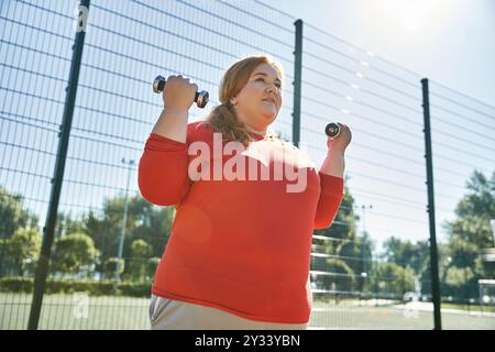 Femme embrasse le fitness, soulevant des haltères à l'extérieur dans un cadre de parc animé. Banque D'Images