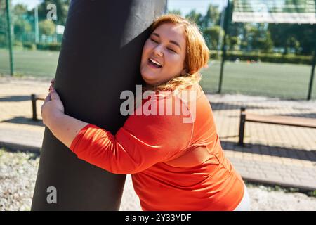 Une femme joyeuse embrasse un poteau de fitness tout en faisant de l'exercice dans le parc. Banque D'Images