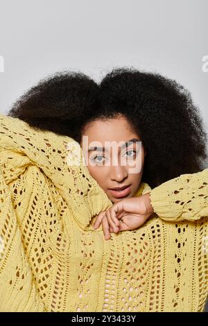 Une jeune femme aux cheveux bouclés présente son style dans un pull jaune vif tout en posant avec confiance. Banque D'Images