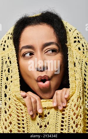 Une jeune femme aux cheveux bouclés pose fantaisiste dans un pull jaune vif, exsudant une énergie ludique. Banque D'Images