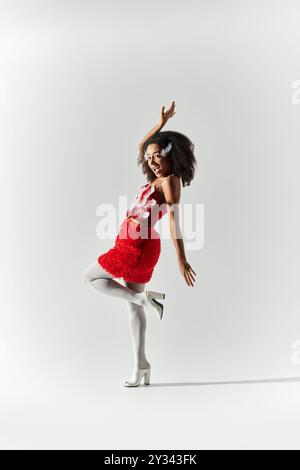 Une jeune femme aux cheveux bouclés pose élégamment dans une tenue rouge éclatante, dégageant confiance et style. Banque D'Images
