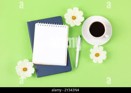 Composition artistique avec bloc-notes vierge ouvert et stylo, tasse de café noir, fleurs d'un cosmos blanc sur fond vert. Bureau festif c Banque D'Images