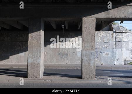 Piliers en béton soutenant un pont, projetant des ombres sur une rue en dessous dans un cadre urbain. Banque D'Images