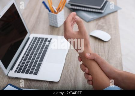 Homme souffrant de douleur au poignet tout en travaillant sur ordinateur portable à la table à l'intérieur, gros plan. Syndrome du canal carpien Banque D'Images