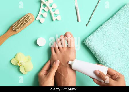 Jeune femme avec une belle pédicure appliquant un produit cosmétique sur fond turquoise Banque D'Images