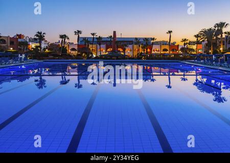 Vue d'une piscine au coucher du soleil avec des reflets de palmiers et de bâtiments dans l'eau dans la ville de Hurghada Banque D'Images