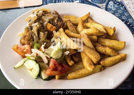 Cuisse de poulet cuite avec frites et légumes sur une assiette blanche et une nappe bleue Banque D'Images