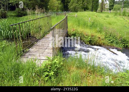 Passerelle en bois et fer sur un cours d'eau dans un paysage de campagne Banque D'Images