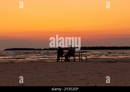 Un couple sur la plage à vérifier leurs téléphones cellulaires alors que le soleil se couche sur le lac Ontario. Banque D'Images