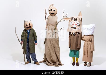 Groupe de personnes portant des masques étranges et des robes surdimensionnées. Tête de citrouille géante, branches de brindilles et masques en papier isolés sur fond blanc Banque D'Images