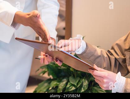 Une femme pointe un document sur un presse-papiers, guidant une autre femme à le signer Banque D'Images