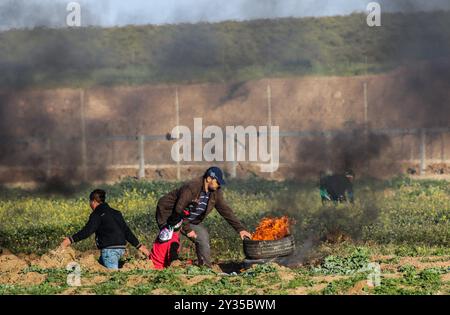 Gaza, Palestine, 8 mars 2019. Des manifestants palestiniens brûlent des pneus et brandissent le drapeau palestinien, quelques pierres lançant vers la clôture, dans la zone de Malika, à l'est de la bande de Gaza. Des manifestants palestiniens s’étaient rassemblés sur différents sites le long de la frontière Gaza-Israël lors de ce vendredi 50ème rassemblement de la Grande Marche du retour, et selon le ministère de la santé à Gaza cinq Palestiniens ont été blessés en ce vendredi mars, dont un dans un état critique. Selon l’armée israélienne, des ballons incendiaires transportant des explosifs ont été lâchés de la bande de Gaza dans le sud d’Israël. La plus haute Comm Banque D'Images