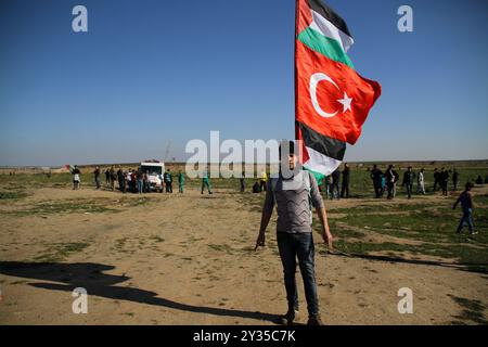 Gaza, Palestine, 8 mars 2019. Des manifestants palestiniens brûlent des pneus et brandissent le drapeau palestinien, quelques pierres lançant vers la clôture, dans la zone de Malika, à l'est de la bande de Gaza. Des manifestants palestiniens s’étaient rassemblés sur différents sites le long de la frontière Gaza-Israël lors de ce vendredi 50ème rassemblement de la Grande Marche du retour, et selon le ministère de la santé à Gaza cinq Palestiniens ont été blessés en ce vendredi mars, dont un dans un état critique. Selon l’armée israélienne, des ballons incendiaires transportant des explosifs ont été lâchés de la bande de Gaza dans le sud d’Israël. La plus haute Comm Banque D'Images