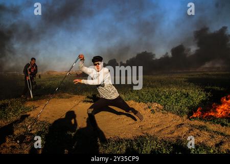 Gaza, Palestine, 8 mars 2019. Des manifestants palestiniens brûlent des pneus et brandissent le drapeau palestinien, quelques pierres lançant vers la clôture, dans la zone de Malika, à l'est de la bande de Gaza. Des manifestants palestiniens s’étaient rassemblés sur différents sites le long de la frontière Gaza-Israël lors de ce vendredi 50ème rassemblement de la Grande Marche du retour, et selon le ministère de la santé à Gaza cinq Palestiniens ont été blessés en ce vendredi mars, dont un dans un état critique. Selon l’armée israélienne, des ballons incendiaires transportant des explosifs ont été lâchés de la bande de Gaza dans le sud d’Israël. La plus haute Comm Banque D'Images