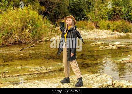 Une fille en vêtements d'automne avec un parapluie se tient sur la rive de la rivière Banque D'Images