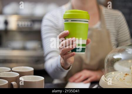 Gros plan d'une travailleuse au café servant du café ou une boisson chaude dans une tasse réutilisable durable Banque D'Images