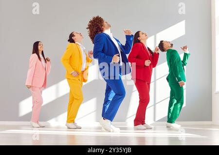 Groupe de jeunes danseurs portant des costumes branchés élégants et lumineux dansant ensemble dans un studio moderne Banque D'Images