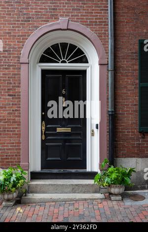 Porte d'entrée noire élégante en Nouvelle-Angleterre. Une élégante porte d'entrée noire encadrée par une voûte gracieuse, faisant une déclaration audacieuse dans le style. Banque D'Images